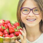 girl with metal braces holding strawberries - Buckeye Pediatric Dentistry in Reynoldsburg