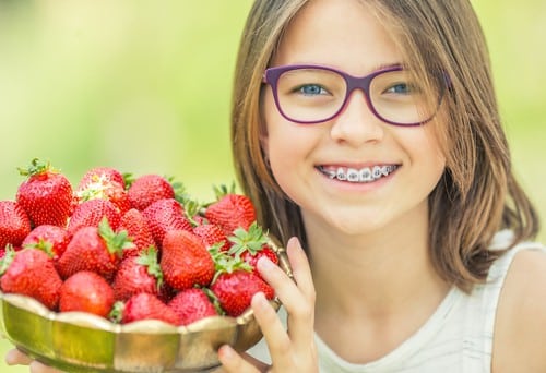 girl with metal braces holding strawberries - Buckeye Pediatric Dentistry in Reynoldsburg